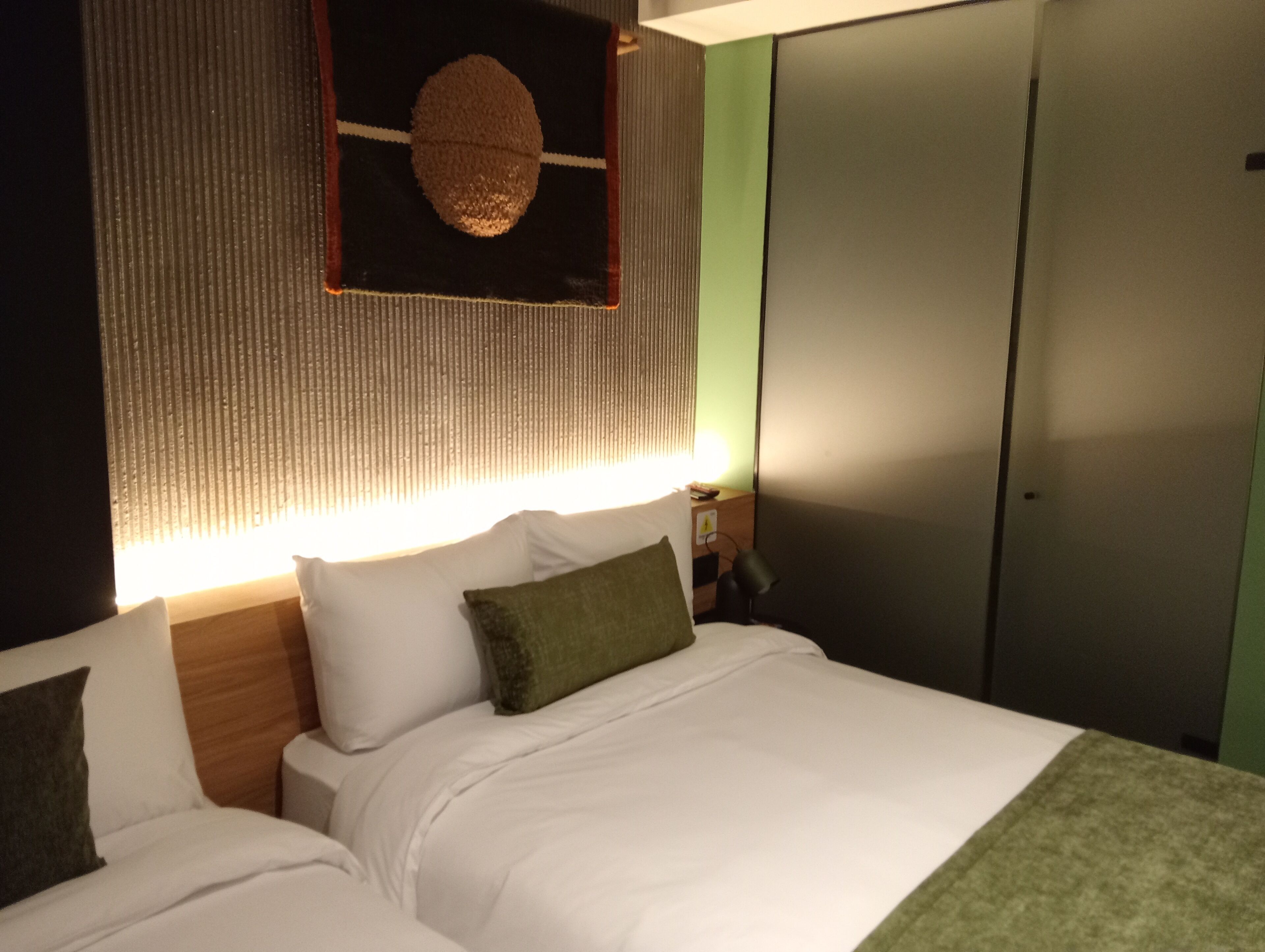 A hotel room with a bed, pillows, a bedside table, a lamp, and a wardrobe.