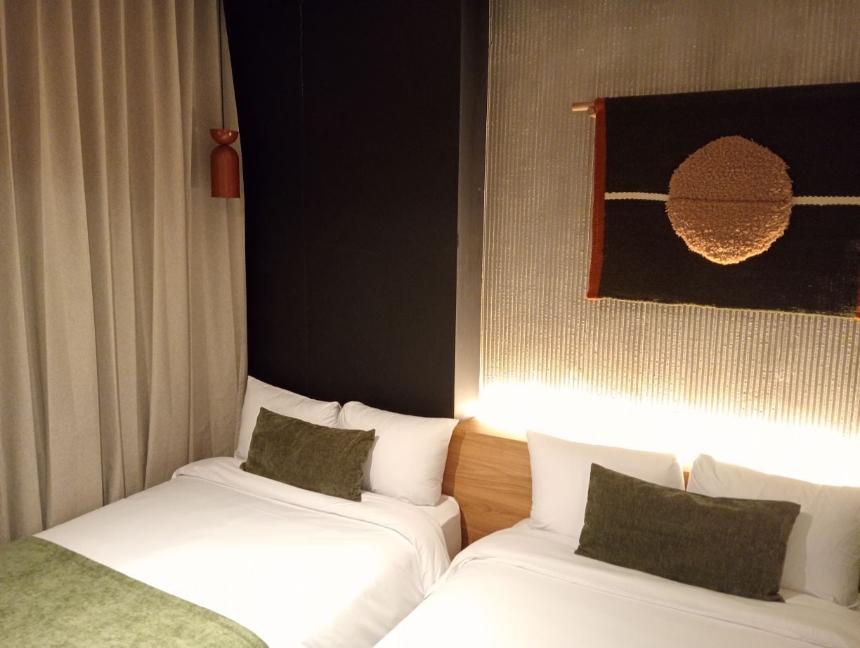A hotel room with two beds, a wall-mounted light fixture, and a curtain.
