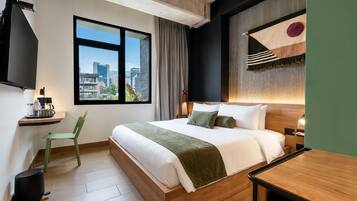 Quarto de hotel moderno com uma cama grande, vista para a cidade, uma mesinha e uma cadeira.