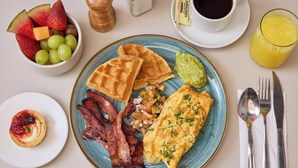 Une assiette de petit-déjeuner comprenant des gaufres, du bacon, des œufs, ainsi qu’une portion de fruits et de guacamole.