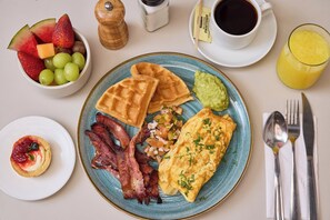 A breakfast plate with waffles, bacon, eggs, and a side of fruit and guacamole. - Hunters Hotel Medellín (Medellín)