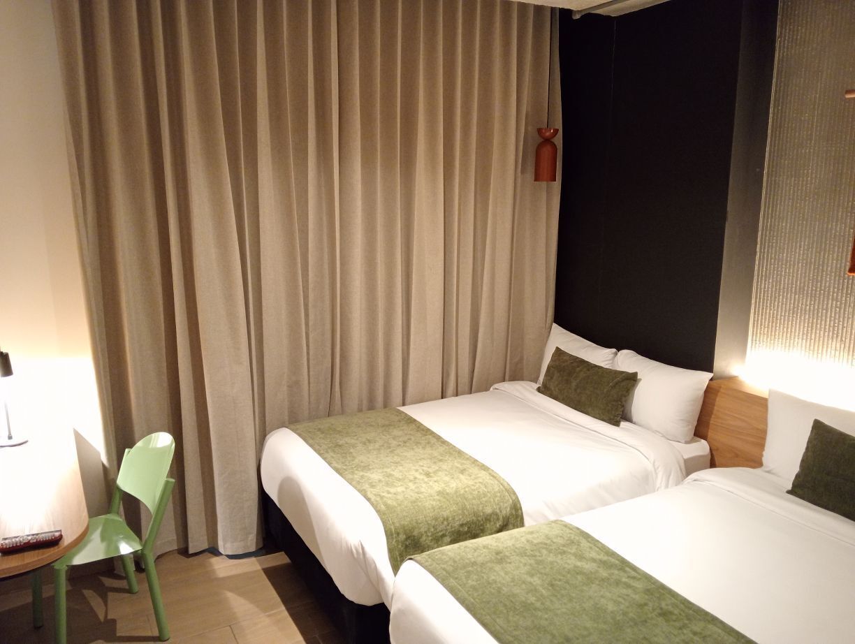 Habitación de hotel con dos camas, un escritorio, una silla y una cortina.