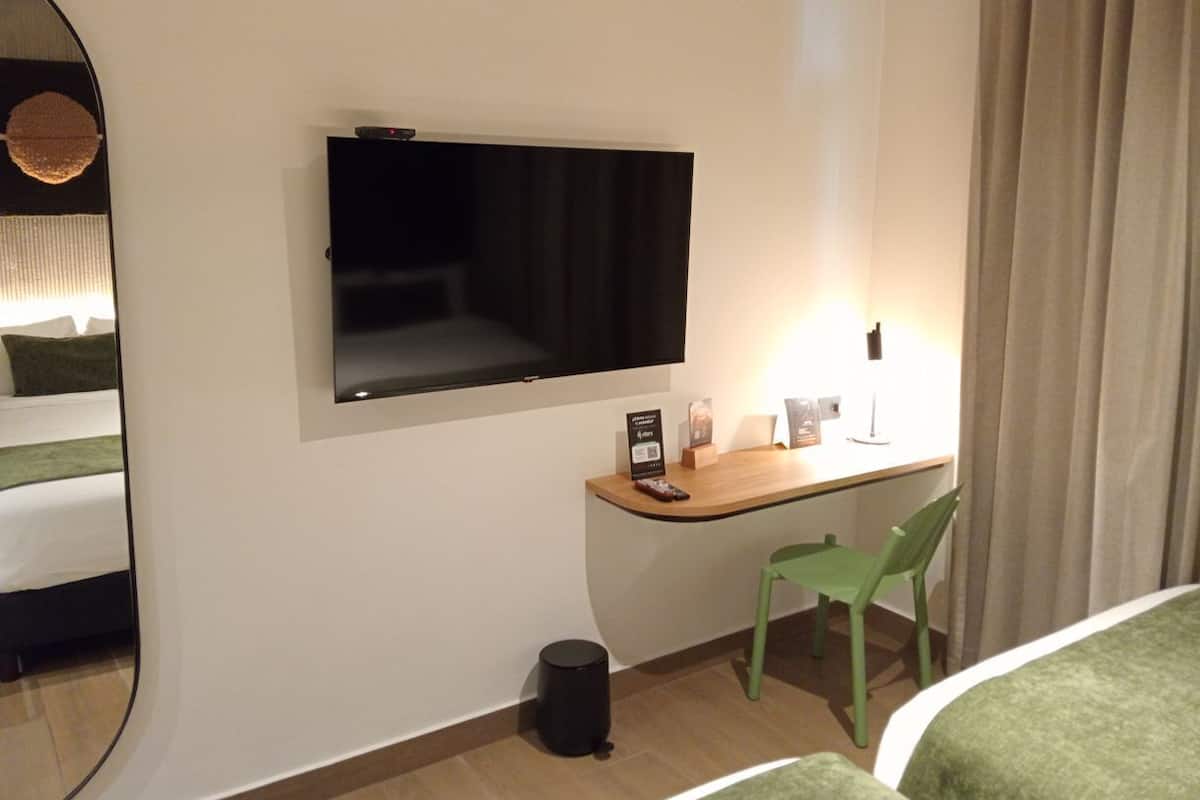 A hotel room with a bed, a desk with a chair, a television, a trash can, and a mirror.