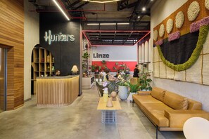 A modern interior with a reception desk labeled 'Hunters,' a seating area with a couch and a table, and a wall with a 'Linze' sign. - Hunters Hotel Medellín (Medellín)