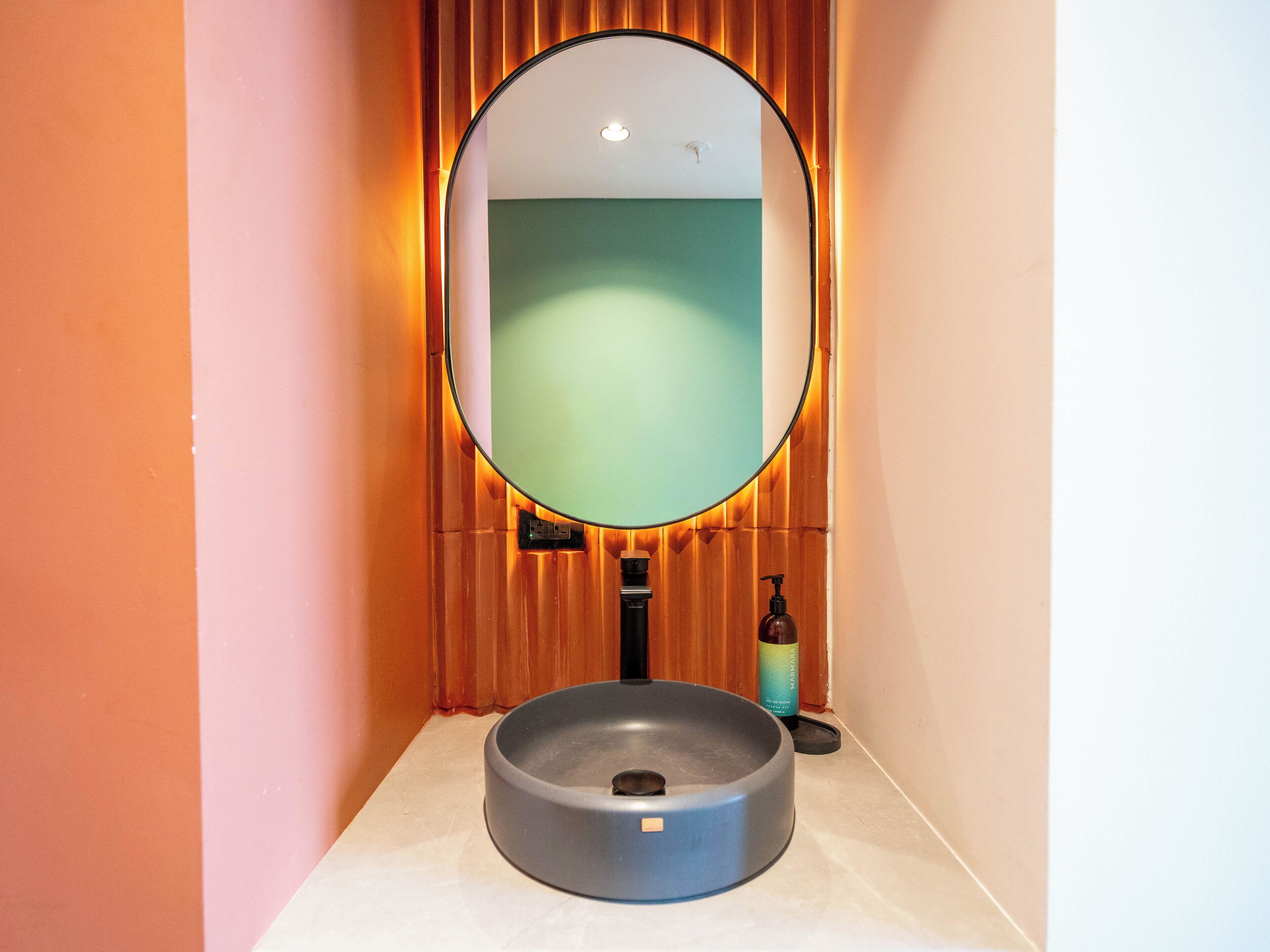 A bathroom with a round sink, a mirror, and a soap dispenser.