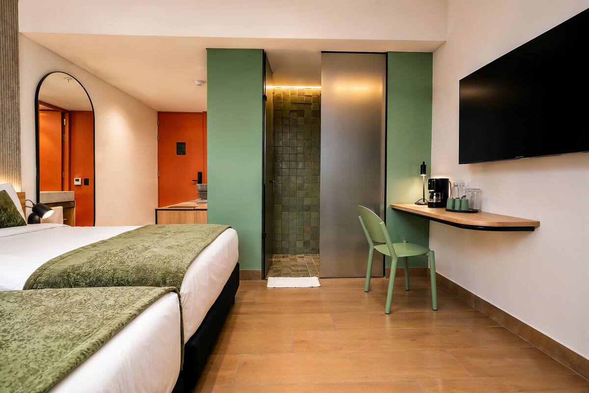 A hotel room with a bed, a chair, a TV, a small table, and a shower area.