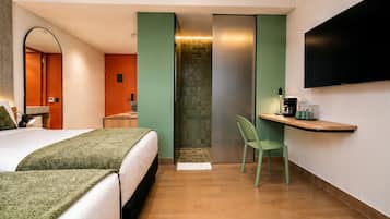 A hotel room with a bed, a chair, a TV, a small table, and a shower area.