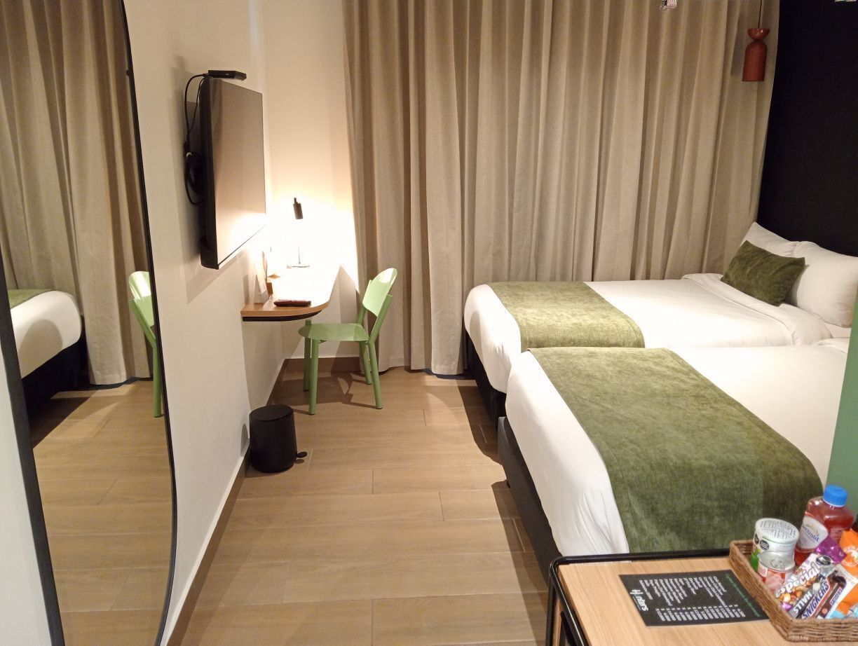 A hotel room with two beds, a desk with a chair, a mirror, and curtains.