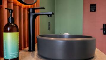 A bathroom with a modern sink, a bottle of shower gel, and a towel rack.