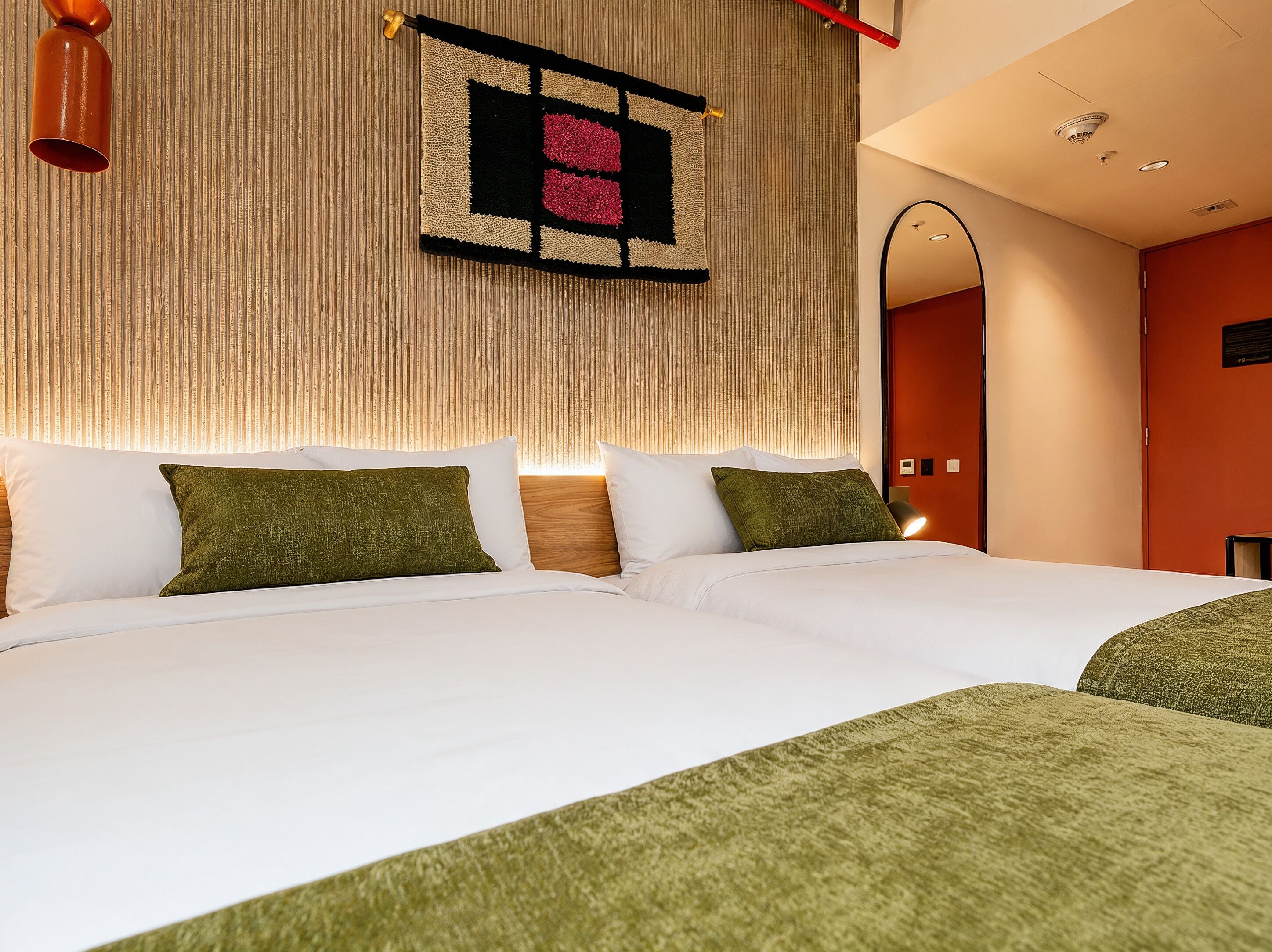 Habitación de hotel con dos camas, una obra de arte en la pared, un espejo y una lámpara en el techo.