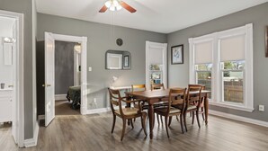 A dining area with a wooden table and chairs, a ceiling fan, and a view of the outside through large windows.