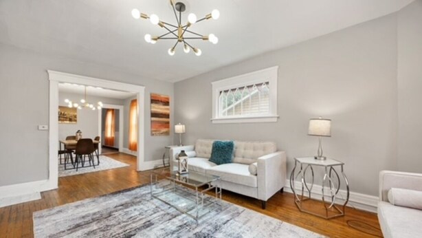 A spacious living room with a white sofa, a coffee table, and a large rug. There is a dining area visible in the background. - Modern 2BR • Mins to Univ, Zoo, Destiny & Downtown (Syracuse)