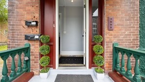 A brick building with a red door, a mailbox, and a green railing. - Modern 2BR • Mins to Univ, Zoo, Destiny & Downtown (Syracuse)