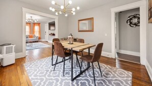 A dining area with a wooden table and chairs, a patterned rug, and a chandelier. - Modern 2BR • Mins to Univ, Zoo, Destiny & Downtown (Syracuse)