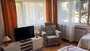 Een slaapkamer met een bed, een stoel, een televisie en gordijnen.