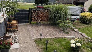 Een woonhuis met een verhard terras, een houten omheining, een schotelantenne en uitzicht op een bergachtig landschap.
