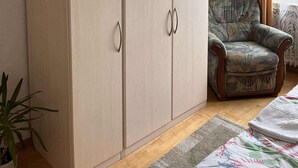 Een kamer met een grote kledingkast, een gestreept fauteuil en een raam met gordijnen.