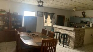 Een eetgedeelte met een houten tafel en stoelen, een keuken met een aanrecht en kastjes, en een betegelde vloer.