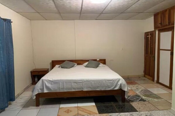 Quarto com cama de madeira, duas mesas de cabeceira, um guarda-roupa e chão estampado.