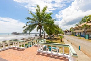 Uma passarela costeira com palmeiras, uma praia e um edifício com fachada azul e branca.