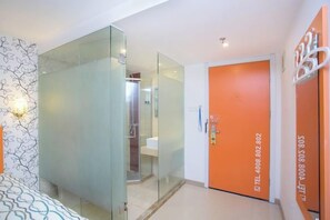 Ein Hotelzimmer mit Glastrennwand, einem Badezimmer mit Dusche und einer orangefarbenen Tür mit Kontaktangaben.