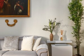 Ein Wohnzimmer mit einer Couch, einem Gemälde, einer Vase mit Blumen und einer hohen, grünen Pflanze.