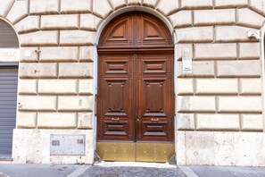 A double wooden door with a brass handle, set in a beige stone wall with a metal vent and a small sign above the door. - Rosam Via Veneto 15 min Walk From Spanish Steps (Rome)