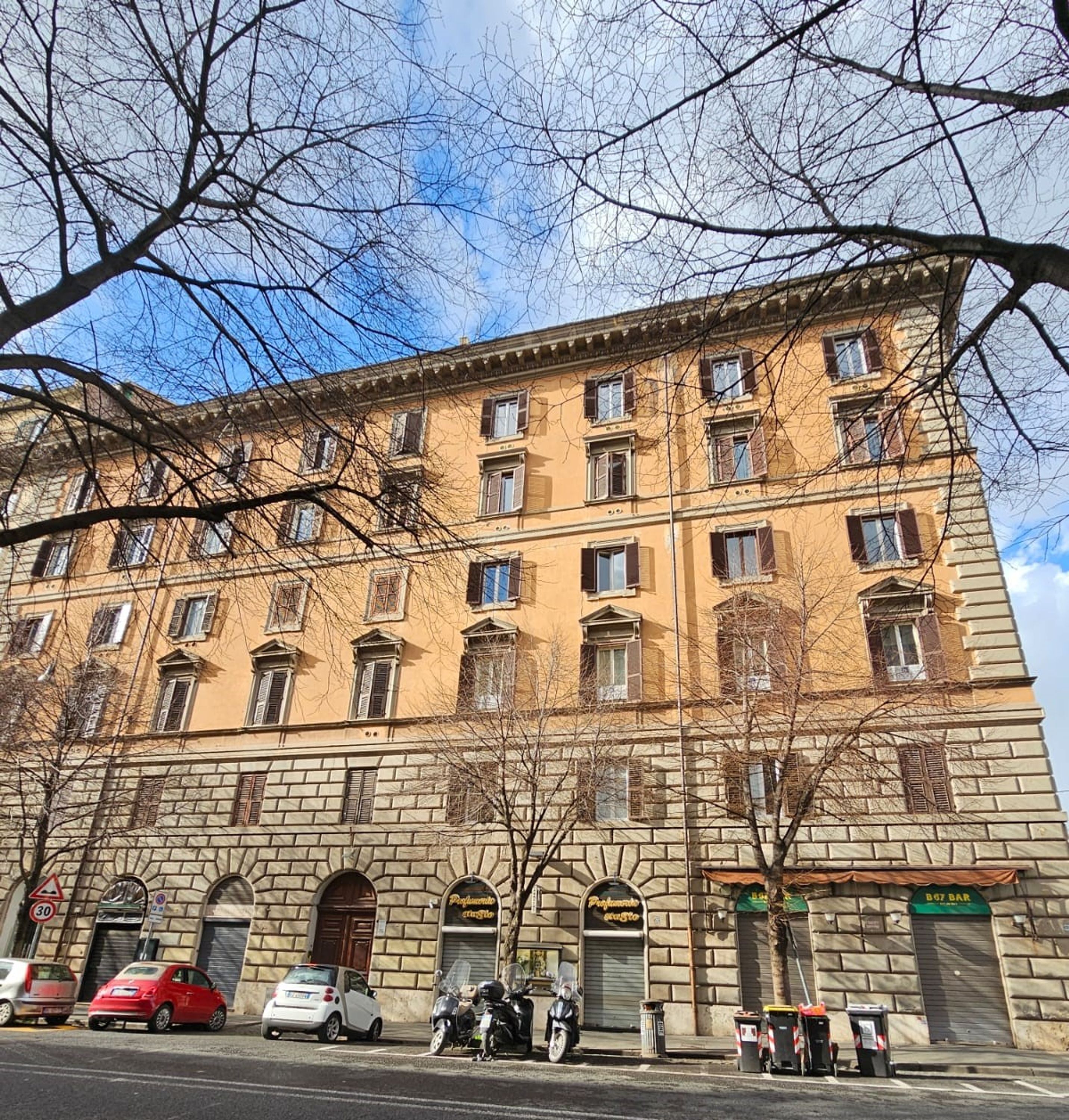 A multi-story building with a stone facade, several windows, and a few parked cars in front.