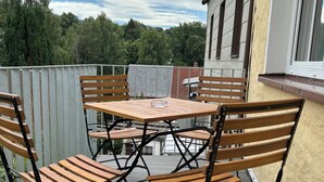 A wooden deck with a table and chairs, a metal railing, and a building in the background. - Exclusive 5-star vacation apartment in the heart of Bischofsgrün (Bischofsgrün)