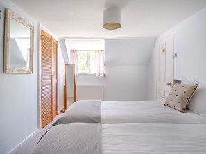 A bedroom with a bed, a window with curtains, a mirror, and a radiator. - Lisle Combe Cottage (Ventnor)