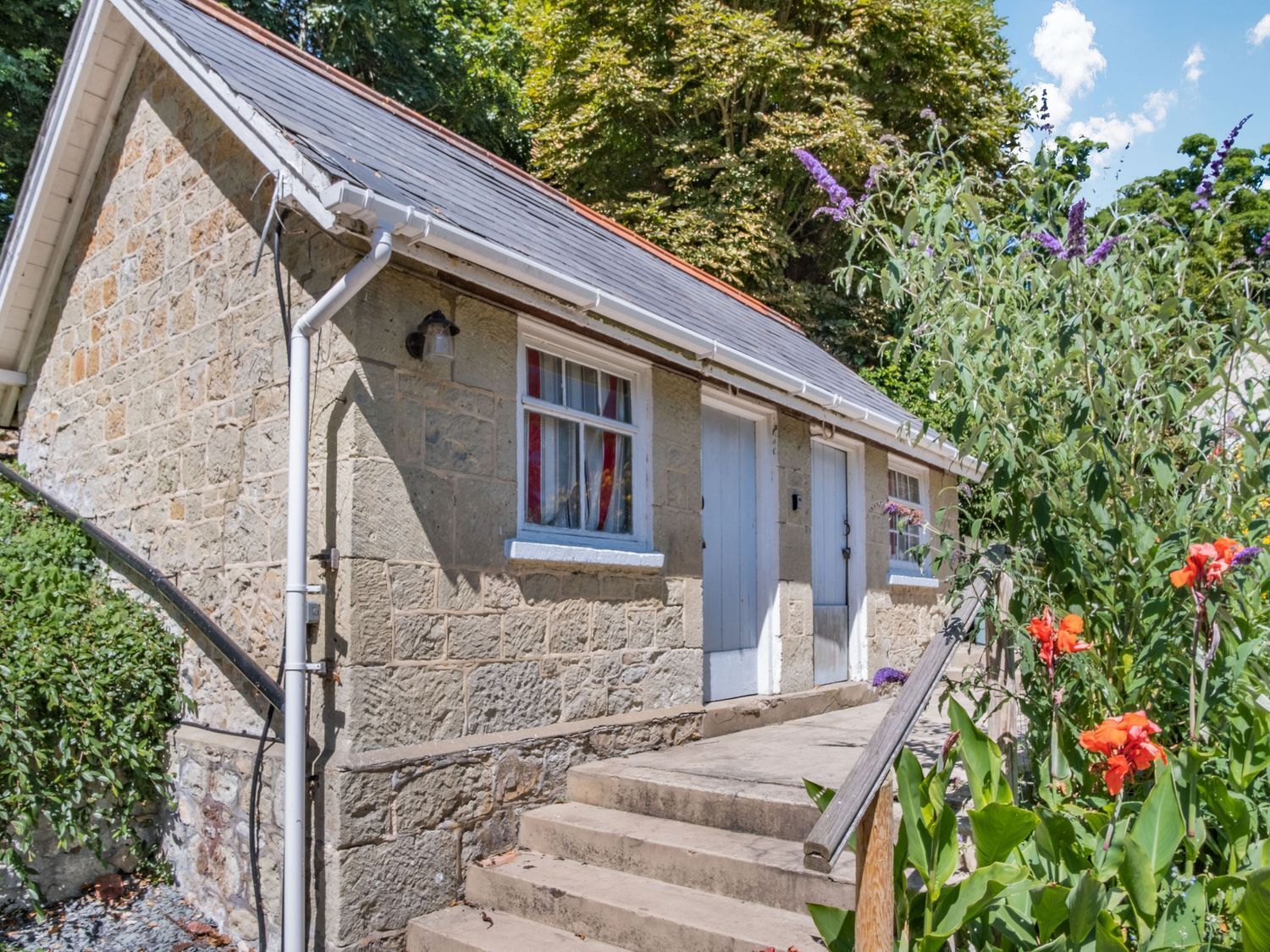 A stone building with a sloped roof and a set of wooden stairs leading to a door.