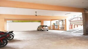 A parking garage with a car and a motorcycle, a ceiling fan, and a green wall. - Hotel Govind Heights (Tirupati)