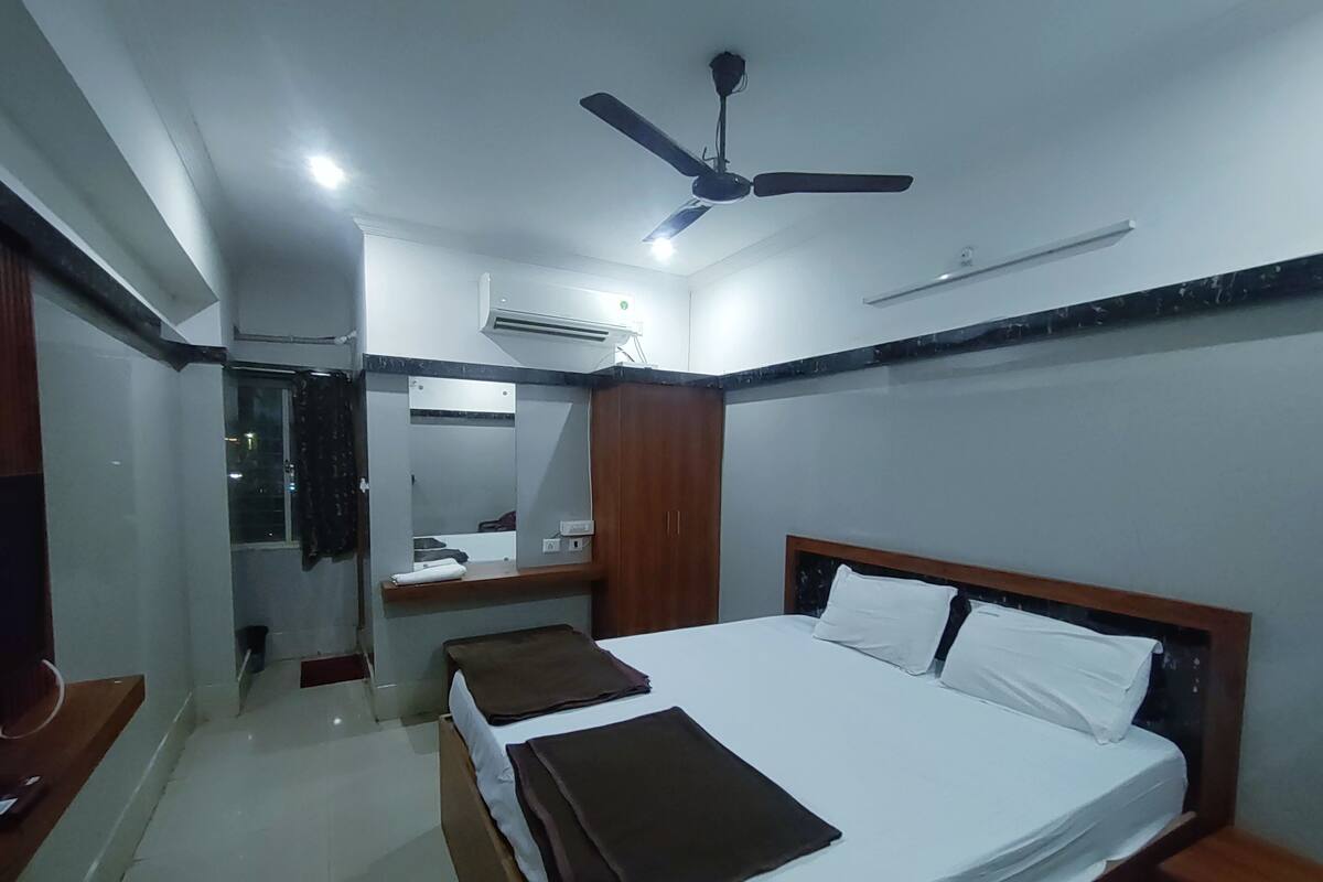 A hotel room with a large bed, a ceiling fan, a mirror, and a small desk.