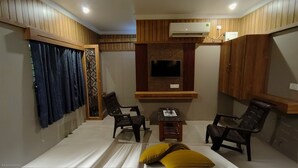 A room with a bed, two chairs, a small table, an air conditioning unit, and a TV mounted on the wall. - Hotel Govind Heights (Tirupati)