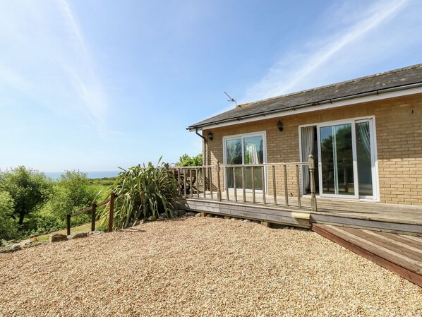 Een huis met een houten terras, een grindpad en uitzicht op zee.