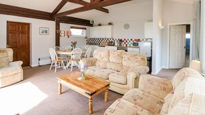 A cozy living room with a wooden ceiling, a dining table with chairs, a sofa, and a kitchen in the background. - Swallows (Ventnor)