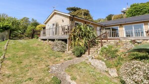 A two-story house with a balcony, a stone pathway, and a garden with various plants. - Swallows (Ventnor)