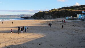A beach with people walking and playing, a lifeguard tower, and cliffs in the background. - Cae Coch (Brynteg)