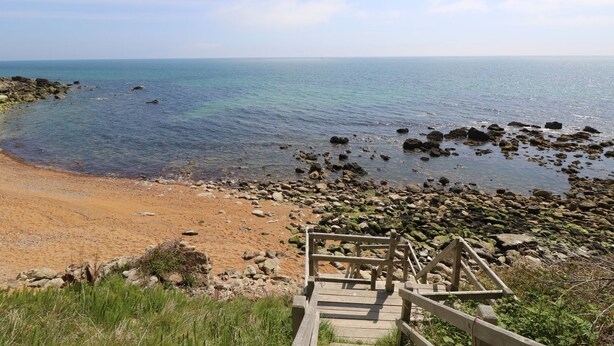 A coastal view with a wooden staircase leading down to a sandy beach and rocky shoreline. - Swifts (Ventnor)