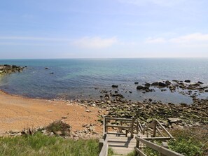 A coastal view with a wooden staircase leading down to a sandy beach and rocky shoreline. - Swifts (Ventnor)