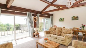 A spacious living room with a wooden ceiling, a sofa, a coffee table, and a dining area with a table and chairs. - Swifts (Ventnor)