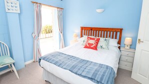 A bedroom with a bed, a chair, a bedside table, and a window with curtains. - Swifts (Ventnor)