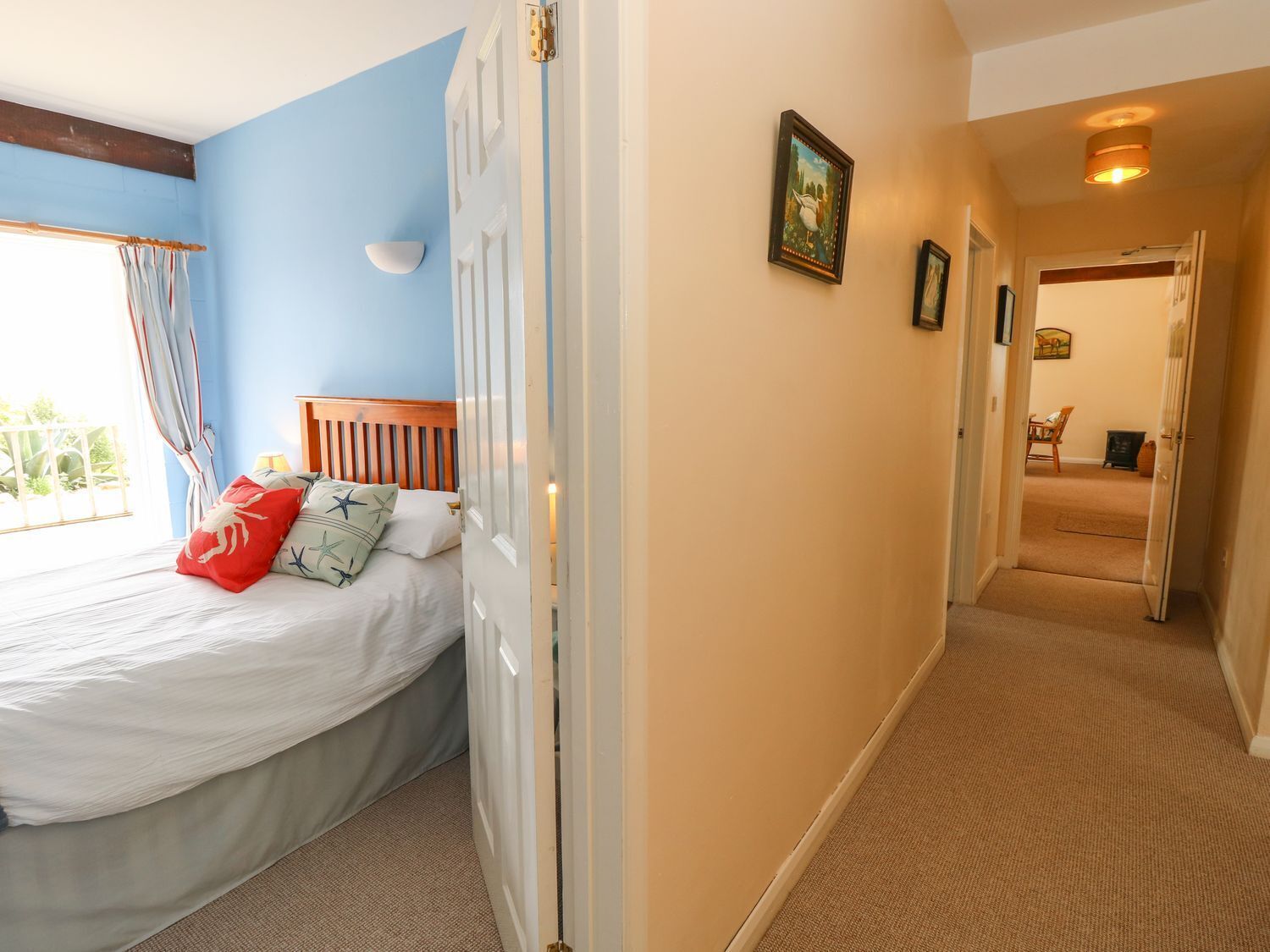 A bedroom with a bed, a window with curtains, a door, and a hallway leading to another room.