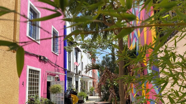 Una calle estrecha con edificios coloridos, una motocicleta estacionada y plantas en macetas.