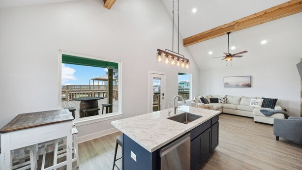 Een moderne keuken met een groot eiland, een eethoek met een houten tafel en een zithoek met een bank en een plafondventilator.