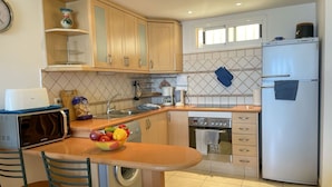 A compact kitchen with wooden cabinets, a built-in oven, a microwave, a sink, and a refrigerator. There is a bowl of fruit on the counter and a washing machine in the corner.