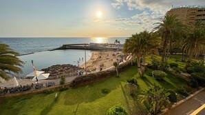 A beach with a rocky breakwater, palm trees, and a building in the background.