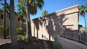 A building with a beige exterior, palm trees, and a paved pathway leading to a gated entrance. - Riverfront Luxury: 4BR Retreat w/ Dock, Launch, Endless Views, Colorado Oasis (Mohave Valley)