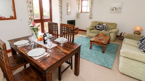 A dining area with a wooden table set for four, a green sofa, and a small coffee table. - The Lobster Pot (Ventnor)