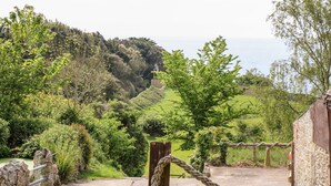 A scenic view of a coastal landscape with lush greenery and a stone building. - The Lobster Pot (Ventnor)